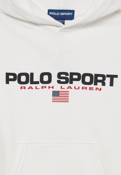 Bela kapuca z natisnjenim besedilom "Polo Sport Ralph Lauren" v črni in rdeči barvi nad majhno grafiko ameriške zastave.