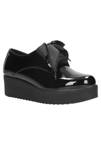 Scarpa con tacco in vernice nera con punta rotonda e un grande fiocco in tessuto sulla parte anteriore. Suola spessa e testurizzata.