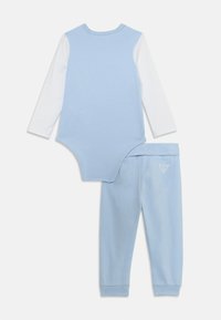 Ensemble pour tout-petit en coton bleu clair avec de longues manches blanches, comprenant un body à fermeture à pression et un pantalon de survêtement assorti bleu avec un détail de logo.