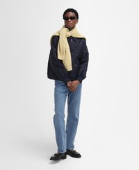 Navy quilted jacket, ribbed cuffs, light yellow knitted scarf, blue straight-leg jeans, and black loafers with gold hardware accents.