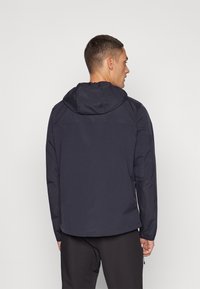 Marineblå hettejakke med en glatt tekstur, som har et enkelt design, lange ermer og justerbare snorer i hetten og nederst.