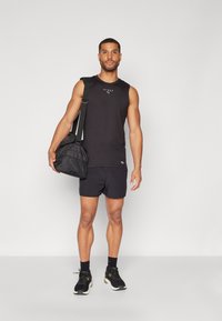 Svart ermeløs tank topp med logo, svarte treningsshorts og svarte sportsko. Bærer en svart treningssekk med skulderrem.
