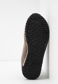 Black rubber sole with textured grip patterns, tan mesh and brown fabric upper, featuring a curved design and minimal stitching details.