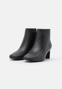 Botines negros de cuero con punta cuadrada y tacón alto, que cuentan con una cremallera lateral y un sutil detalle de costura a lo largo de las costuras.