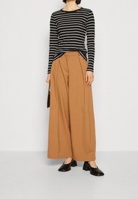 Maglietta a righe bianche e nere a maniche lunghe abbinata a pantaloni a vita alta, beige, a gamba larga. Scarpe con tacco blocco nere completano l'outfit.
