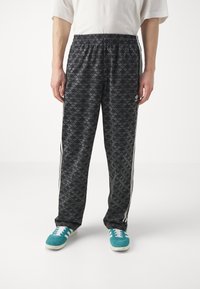 Svarta sportbyxor med ett upprepande mönster av mörkgrå logotyp, elastisk midja, vita sidostråk och ihopparade med turkosa sneakers.