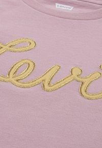 T-shirt rosa chiaro con un grande logo "Levi's" ricamato in oro sul davanti, che mette in mostra uno stile di moda casual.