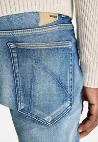 Helle blaue Jeans aus Denim mit einem einzigartigen dreieckigen Taschendesign, kontrastierenden Nähten und einem Lederetikett mit "CHASIN'" am Bund.