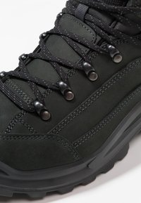 Bota de senderismo negra hecha de ante y materiales sintéticos, con cordones duraderos, ojales metálicos y suela de goma texturizada con patrones de tracción.