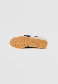 Talpa de pantof de sport negru, cu o talpă din cauciuc texturat, având un model de fagure și gripuri circulare, înconjurată de o margine de culoare crem.