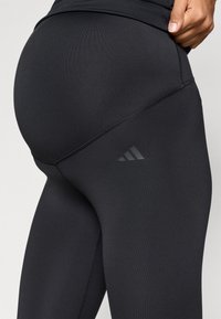 Μαύρα αθλητικά κολάν από ελαστικό ύφασμα, με λεία υφή και διακριτικό λογότυπο Adidas στο πλάι. Το ραφή χωρίς ραφές βελτιώνει τη εφαρμογή.