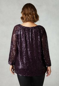 Maglietta a maniche lunghe viola ricoperta di paillettes, con scollatura arricciata e vestibilità ampia con orlo arrotondato, abbinata a pantaloni neri.