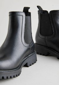 Botas Chelsea de cuero negro con paneles laterales elásticos, acabado texturizado, suelas bajas de goma gruesa y lengüetas en el tobillo para facilitar su uso.