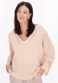 Halvány rózsaszín kötött kapucnis pulcsi V-nyakkal, hosszú ujjakkal és laza szabással. Figyelemre méltó textúrájú, könnyű, légies anyag.