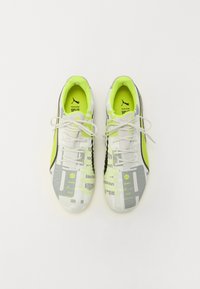 Zapatillas deportivas en blanco y gris con un acento verde, diseño texturizado, punta redonda y cordones, que incluyen una marca en la lengüeta y en los laterales.