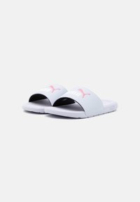 Saboti albi cu un brâu capitonat, având un logo roz Puma. Talpa este texturată pentru aderență, cu un design rotunjit și minimalist.