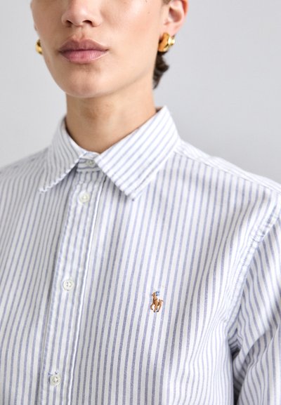 Chemise à rayures bleues et blanches, dotée d'un col classique et d'un petit logo brodé sur le côté gauche. Coupe ajustée, en coton.