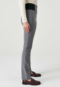 Pantalon ajusté gris avec une coupe élégante, ceinture élastique noire et texture douce. Fini avec des coutures détaillées le long des côtés.