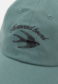 Zöld pamut sapka fekete hímzett szöveggel és fecske mintával az elején. Az anyag texturált, bordázott felülettel rendelkezik.