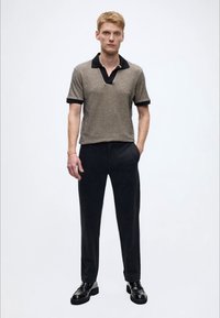 Polo castanho texturizado com colarinho preto, combinada com calças pretas e sapatos pretos. Design simples e moderno, mangas curtas.