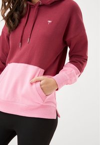 Hooded sweatshirt featuring a color-block design in deep red and pink, with a front pocket, drawstring, and side slits at the hem.