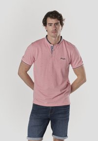 Roosa polo-särk lühikese nööbitava kraega, millel on väikesed mereväe aksendid ja mustrid, sobitatud siniste teksapükstega.