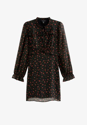 Robe noire à fleurs avec manches longues, taille cintrée, accents volants, et petits motifs de fleurs rouges sur un tissu transparent. Encolure arrondie.