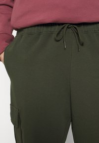 Khaki groene sweatpants met een trekkoord in de taille, zijzakken en een zachte textuur. Gecombineerd met een paarse sweatshirt aan de bovenkant.