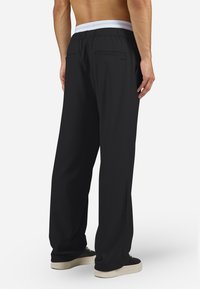 Fekete, laza szabású nadrág fehér gumis derékpánttal, két hátsó zsebbel és sima, könnyű anyagból.