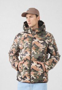 Piumino con motivo mimetico in tonalità di verde, marrone e beige; dotato di cappuccio, chiusura a zip e tasche laterali.