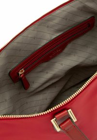 Interno di una borsa in pelle rossa con una fodera grigia caratterizzata da sottili righe diagonali, una tasca con zip e accessori in oro lungo la zip.