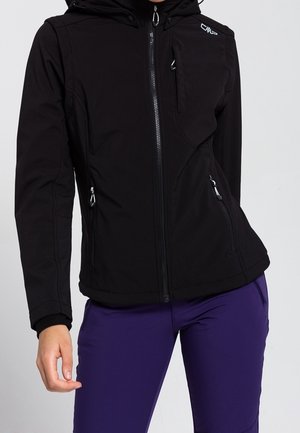 Veste noire zippée avec capuche et poche poitrine, portée avec un pantalon violet ; logo visible sur la partie supérieure droite de la poitrine.