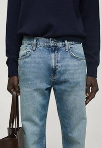 Jeans de mezclilla azul claro con corte recto, acabado desgastado, cinco bolsillos y trabilla en la cintura, combinados con un suéter oscuro.