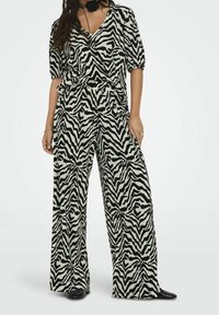 Jumpsuit se zebřím potiskem v černé a krémové, s výstřihem do V, krátkými nabíranými rukávy, širokými nohavicemi a měkkou texturou látky.