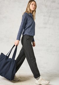 Marineblauw patroon overhemd met lange mouwen, grijze taps toelopende joggers en witte sneakers. Draagt een grote marineblauwe tote bag. Eenvoudige, casual outfit.