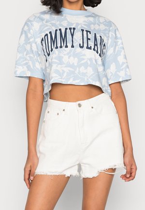 Lyseblå cropped t-shirt med hvidt blomsterdesign og "TOMMY JEANS" tryk, parret med hvide denimshorts med frynset kant og lommer.