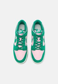 Ett par gröna och rosa Nike-sneakers med snören, sedd ovanifrån på en enkel vit bakgrund.