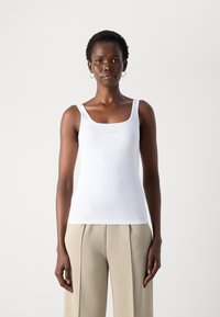Witte geribde tanktop met brede bandjes, met een vierkante halslijn en een klein logo op de voorkant, gecombineerd met beige wijde broekspijpen.