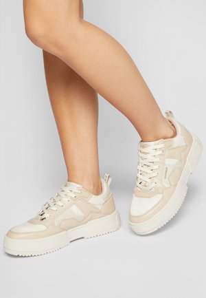 Beige sneakers with a mix of matte and shiny textures, featuring lace-up closure, a thick sole, and side accents in matching tones.