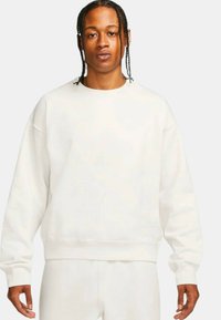 White crewneck sweatshirt made of soft fabric, featuring loose fit, ribbed cuffs, and a small logo detail on the chest.