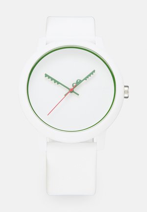 Reloj de silicona blanco con esfera redonda, marcadores de hora verdes, segundero rojo y un acento verde en el bisel. Correa texturizada blanca.