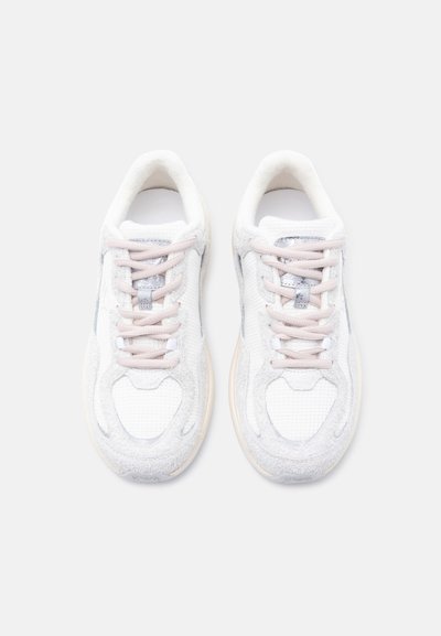 Ζευγάρι λευκών και ανοιχτόγκρι αθλητικών παπουτσιών με υφή και κορδόνια σε ροδακινί-μπεζ απόχρωση, σε θέα από ψηλά σε απλό λευκό φόντο.