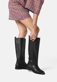 Black knee-high boots made of smooth leather with a sleek design, featuring a subtle metallic accent on the toe and pull tabs for easy wear.