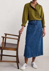 Blouse à carreaux verts avec col à volants, associée à une jupe en jean bleue taille haute avec deux poches. Baskets blanches avec touches violettes.