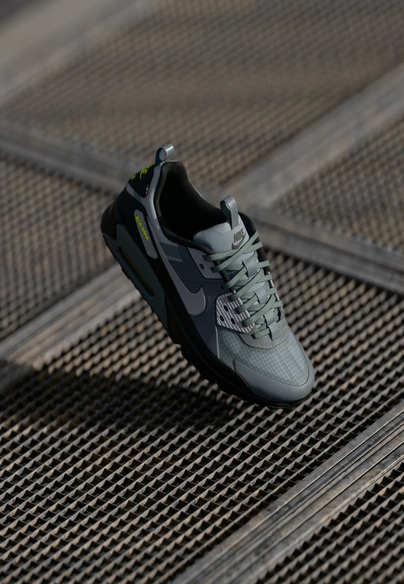 Nike Air Max sneaker in gray with black accents, textured mesh upper, lace-up design, and visible air cushion. Reflective details in the design.