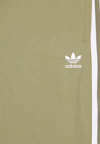 Khakigrön tyg med vit Adidas trefoil-logotyp och vertikala vita och gröna ränder på högra sidan.