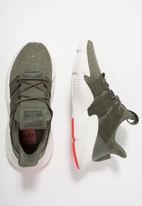 Gröna stickade sneakers med en texturerad ovandel, vit sula och orange accent. Har ett snörningsdesign och perforerade sidopaneler.