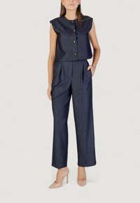 Námořnická modrá bezrukávová cropped top s kulatým výstřihem a třemi knoflíky, spárovaná s kalhotami s širokými nohavicemi, které mají sklady na přední straně a kapsy.