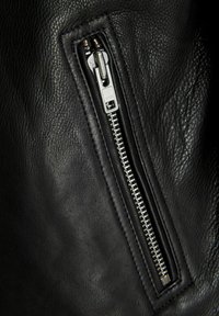 Close-up of a silver metal zipper on a textured black leather fabric surface.