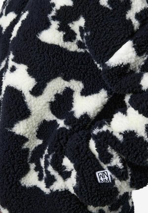 Schwarze und weiße Fleece-Jacke mit einem weichen, strukturierten Kuhfleckenmuster und einem kleinen Marken-Logoschild an der Seite.